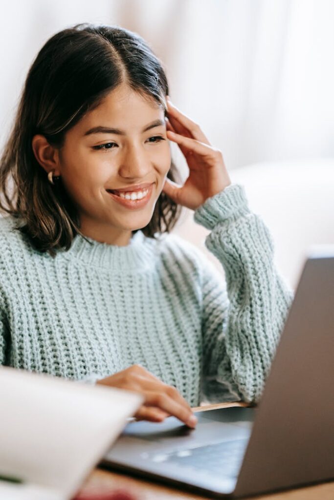 Hispanic woman working remotely on laptop near notepad in apartment